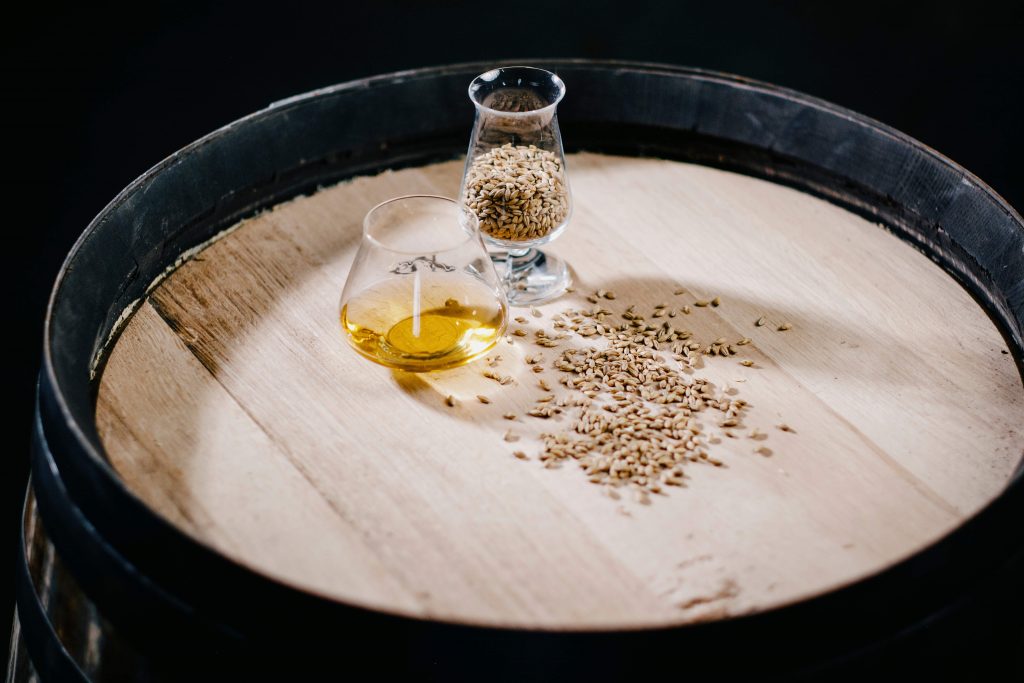 A whiskey dram on a barrel surrounded by barley
