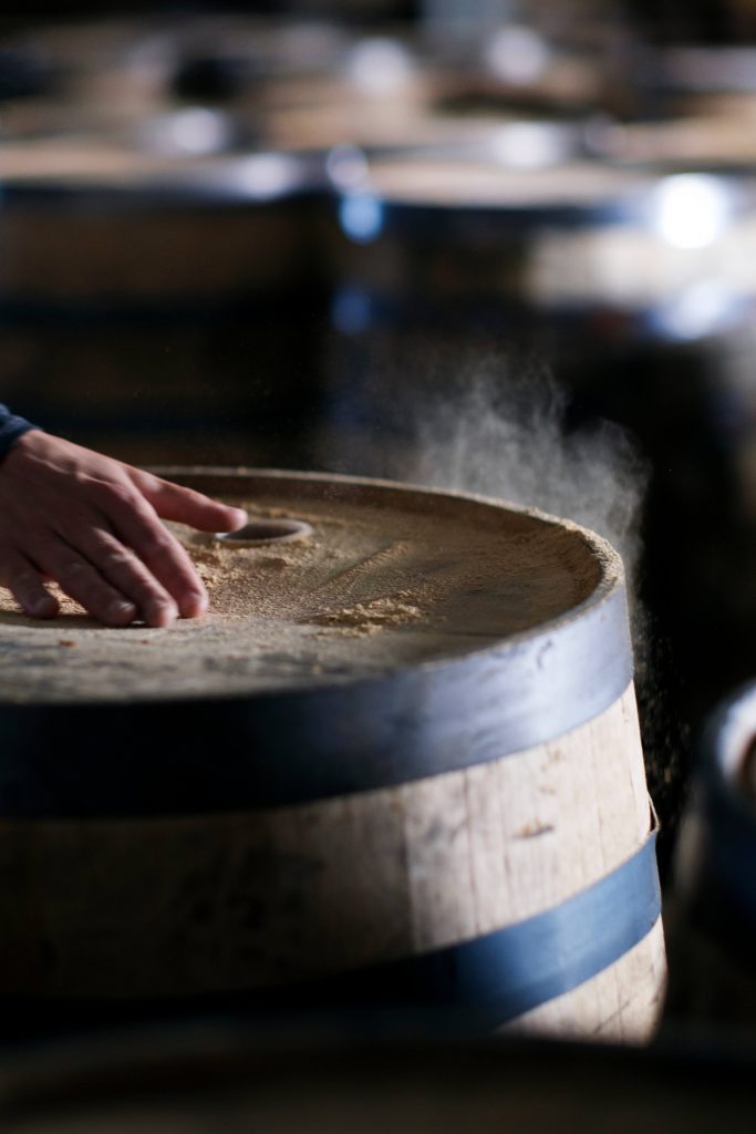 A hand brushing off sawdust from a wooden cask